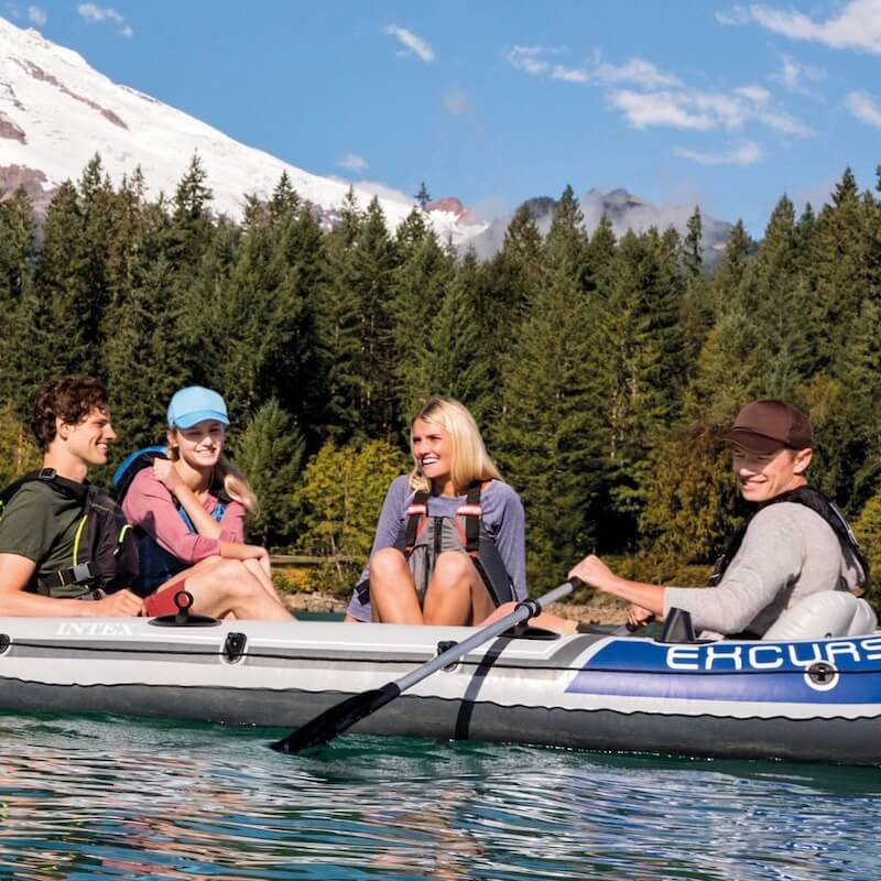 Four people in an inflatable boat on a lake with mountains in the background