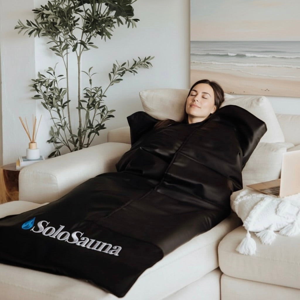 Person lying on a black sauna blanket with 'SoloSauna' branding on a couch.