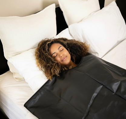 Woman sleeping under a black sauna blanket on a bed with white pillows