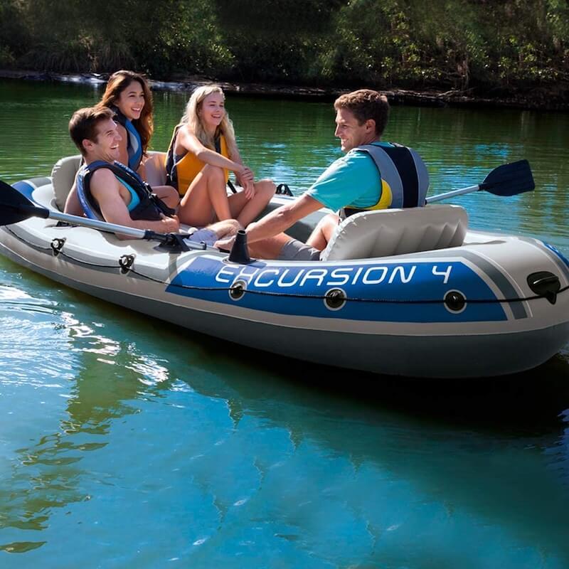 Four people in an inflatable kayak labeled 'Excursion 4' on a calm body of water.