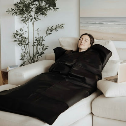 Person lying on a black sauna blanket on a couch.